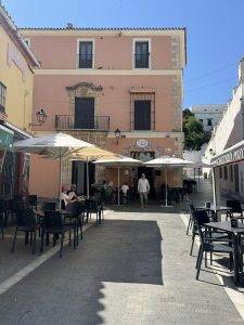 Kopfsteinpflasterplatz vor rosa Gebäude mit Außensitzbereichen Plaza de San Roque