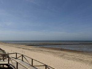 Weitläufiger Strand mit Holzsteg bei Ebbe Die Corralles bei Niedrigwasser